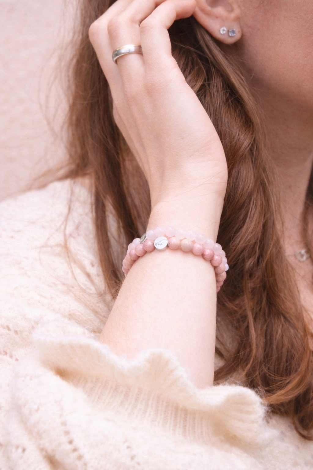 arm met rozenkwarts en rhodoniet armband, waarbij de hand door het haar van een vrouw gaat